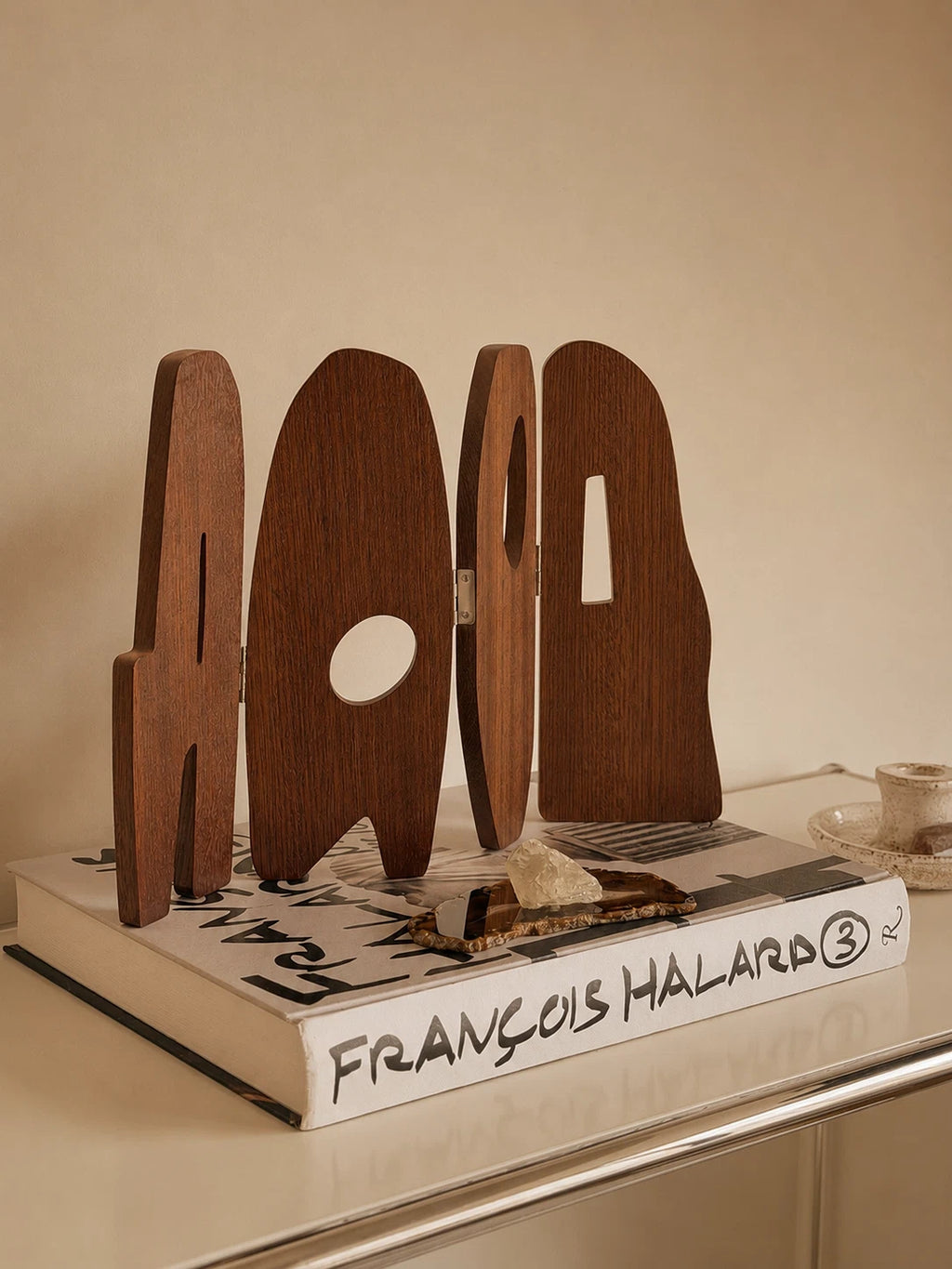 Handcrafted solid wood folding screen sculpture with curved panels and geometric cutouts displayed on stacked art books.
