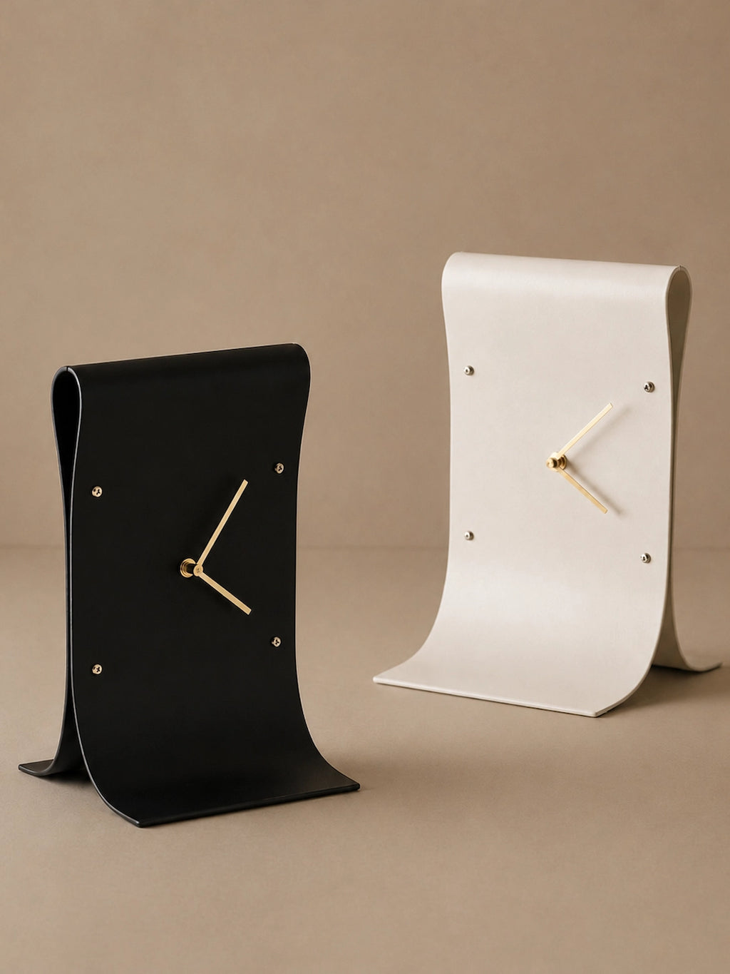 Black and white curved table clocks with gold-tone hands against a neutral beige background.